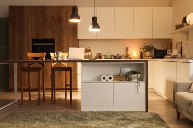 Akşam vakti mutfak masası, tezgahlar ve parlayan lambalar.