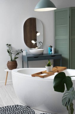 Banyonun içinde küvet, yeşil bitkiler ve parlayan lamba var.