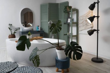 Banyonun içinde küvet, yeşil bitkiler ve parlayan lamba var.