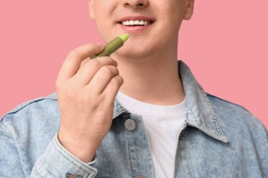 Pembe arka planda dudak merhemi olan genç adam, yakın plan.