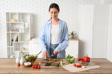 Mutfakta taze sebze salatası hazırlamak için salatalık kesen genç ve güzel bir kadın.