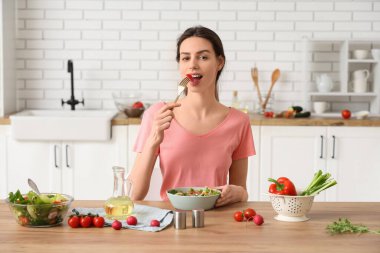 Genç ve güzel bir kadın mutfaktaki masada taze sebze salatası yiyor.