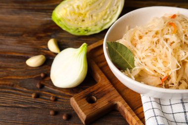 Lezzetli lahana turşusu kasede ve ahşap arka planda malzemeler