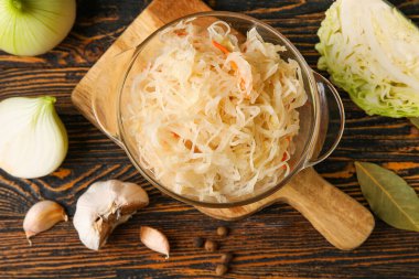 Ev yapımı lahana turşusu ve ahşap masadaki malzemelerle dolu bir kase.