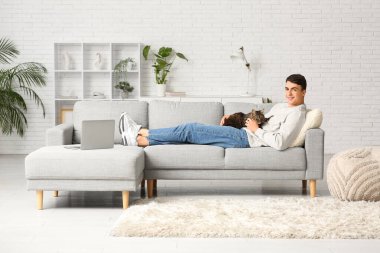 Evdeki kanepede tatlı kedili genç bir adam yatıyor.