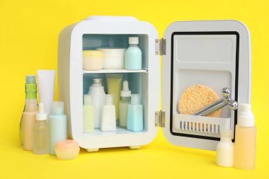 Sarı arka planda kozmetik ürünleri olan küçük bir kozmetik buzdolabı.