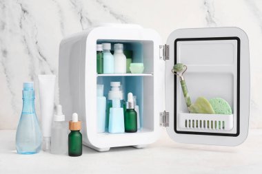 Mermer duvarın yanında kozmetik ürünleri olan küçük bir kozmetik buzdolabı.
