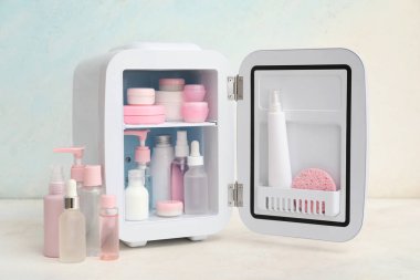 Açık mavi arka planda kozmetik ürünleri olan küçük bir kozmetik buzdolabı