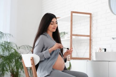 Genç hamile kadın evde makyaj yapıyor.