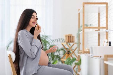 Genç hamile kadın evde makyaj yapıyor.