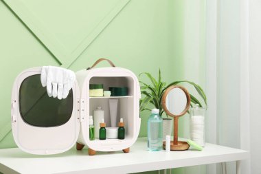 Kozmetik ürünleri, tıbbi eldivenler ve yeşil duvarda ayna olan küçük buzdolabı.