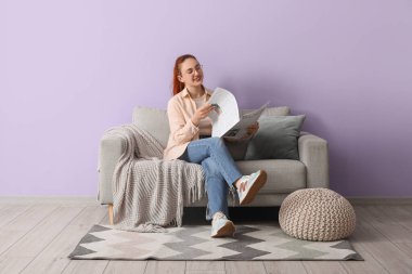 Evdeki rahat koltukta gazete okuyan genç bir kadın.