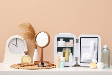 Kozmetik ürünleri, ayna ve saati olan küçük buzdolabı kahverengi duvara karşı.