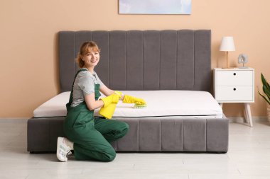 Kadın hademe yatak odasında fırça ve deterjan ile yatağı temizliyor.