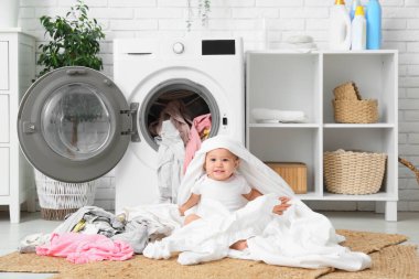 Çamaşırhanede kıyafetlerle oynayan tatlı çocuk.