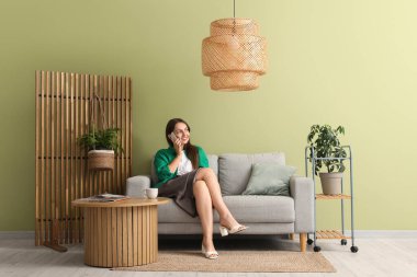 Evdeki gri koltukta cep telefonuyla konuşan genç ve güzel bir kadın.