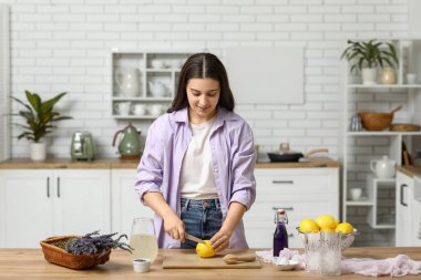 Mutfaktaki masada lavantalı limonata hazırlamak için limon kesen genç bir kadın.