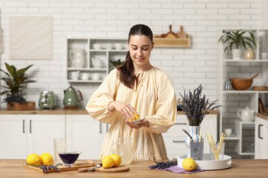 Mutfaktaki masada lavantalı limonata hazırlamak için meyve sıkacağı sıkan genç bir kadın.