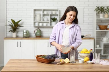 Mutfaktaki masada lavanta limonatası hazırlamak için limon suyunu bardağa dolduran genç bir kadın.