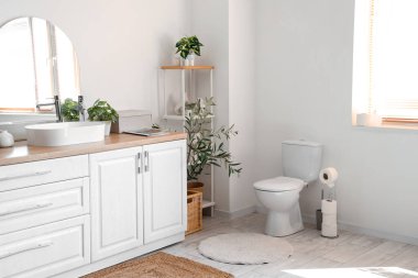 Modern klozeti olan modern tuvaletin şık iç mekanı, lavabosu, aynası ve raf ünitesi olan tezgah.