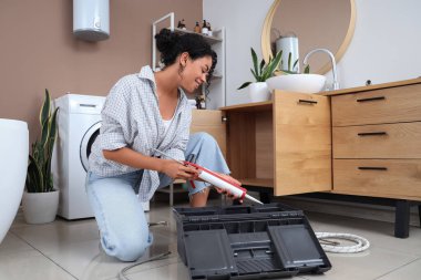 Kadın Afro-Amerikalı tesisatçı banyodan tutkal tabancası alıyor.