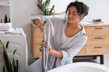 Kadın Afro-Amerikalı tesisatçı banyoda banyo musluğu tamir ediyor.