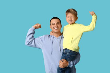 Mutlu baba ve küçük oğlu mavi arka planda kaslarını gösteriyor.