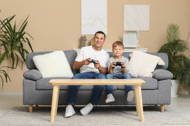 Mutlu baba ve küçük oğlu evdeki kanepede oyun oynuyorlar.