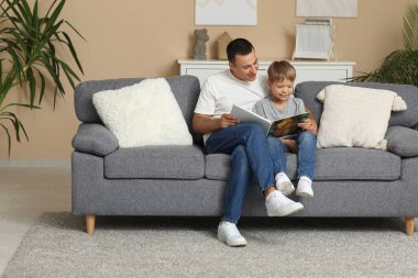 Mutlu baba ve küçük oğlu evdeki kanepede kitap okuyorlar.