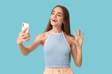 Diastemalı genç bir kadın mavi arka planda selfie çekiyor.