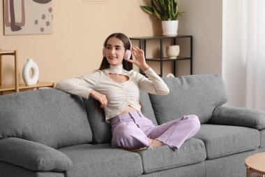 Kulaklık takan, diyabetik hastası, evdeki kanepede oturan genç bir kadın.