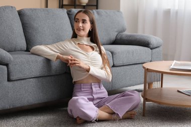 Diastemalı genç bir kadın evde yerde oturuyor.