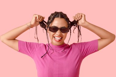 Pembe arka planda dilini gösteren siyah saçlı güzel bir Afro-Amerikalı kadın.