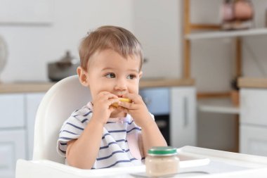 Bir kavanoz lezzetli yiyeceği olan sevimli bir bebek. Evdeki mutfakta sandalyede meyve yiyor.