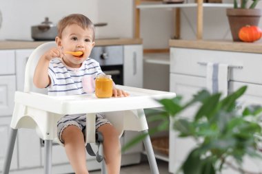 Evdeki mutfaktaki sandalyede yemek yiyen tatlı küçük bir bebek.