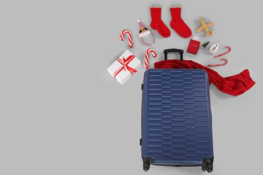 Noel aksesuarlarıyla dolu bavul ve gri arka planda ahşap uçak. Seyahat konsepti. Üst görünüm