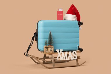 Kızaklı bavul, XMAS kelimesi, mini Noel ağacı ve bej arka planda Noel Baba şapkası. Seyahat kavramı