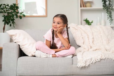 Evdeki kanepede oturan düşünceli küçük kız.