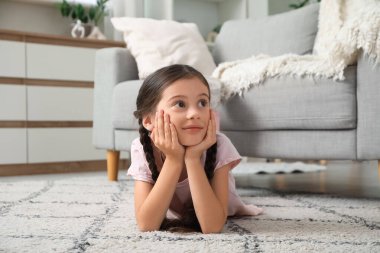 Evdeki halıya uzanmış düşünceli küçük kız.