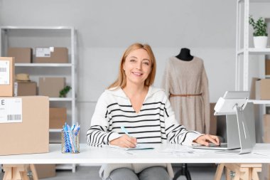 Online mağaza deposunda dizüstü bilgisayarla çalışan bir kadın satıcı.