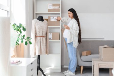 Online mağaza deposunda tablet bilgisayar ve paket ile çalışan hamile satıcı