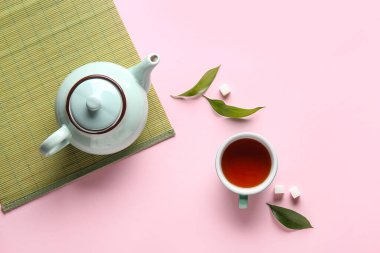 Pembe arka planda çay demliği, çay fincanı ve bambu paspası olan güzel bir kompozisyon.