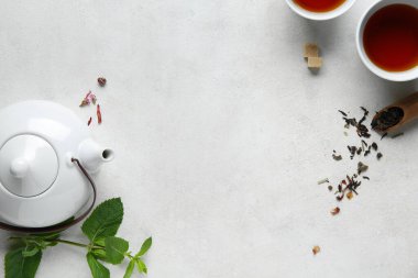 Çay demliğinden yapılmış çerçeve, çay fincanları ve açık arkaplanda yeşil yapraklar.