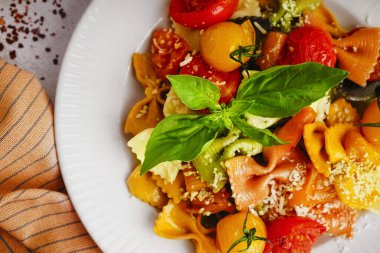 Beyaz arka planda domates ve fesleğenli lezzetli farfalle makarna tabağı, yakın plan.