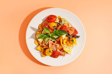 Turuncu arka planda domates ve fesleğenli bir tabak lezzetli farfalle makarna.