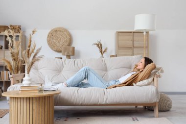 Evdeki bej kanepede uzanan genç bir kadın.