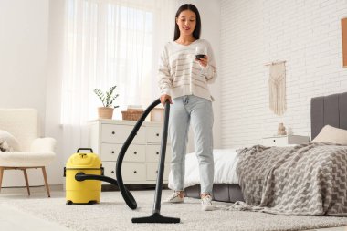 Genç Asyalı kadın yatak odasını bir bardak şarapla süpürüyor.