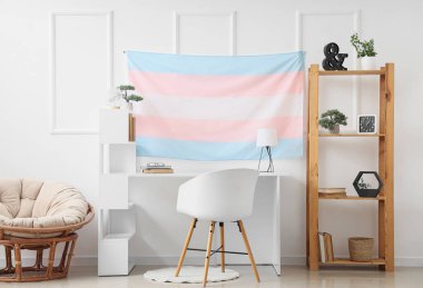 Masa, raf ünitesi ve transseksüel bayrağı asılan modern işyeri.