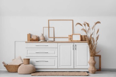 Beyaz duvarın yanında farklı ev dekorasyonu ve kuru kamış vazosu olan şık bir tuvalet.