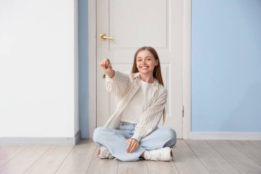 Anahtarları olan güzel genç bir kadın yeni evinin kapısında oturuyor.